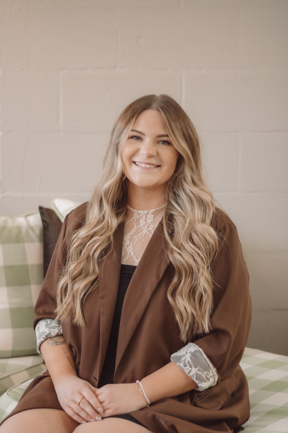 Smiling woman in a brown blazer seated on a green checked sofa