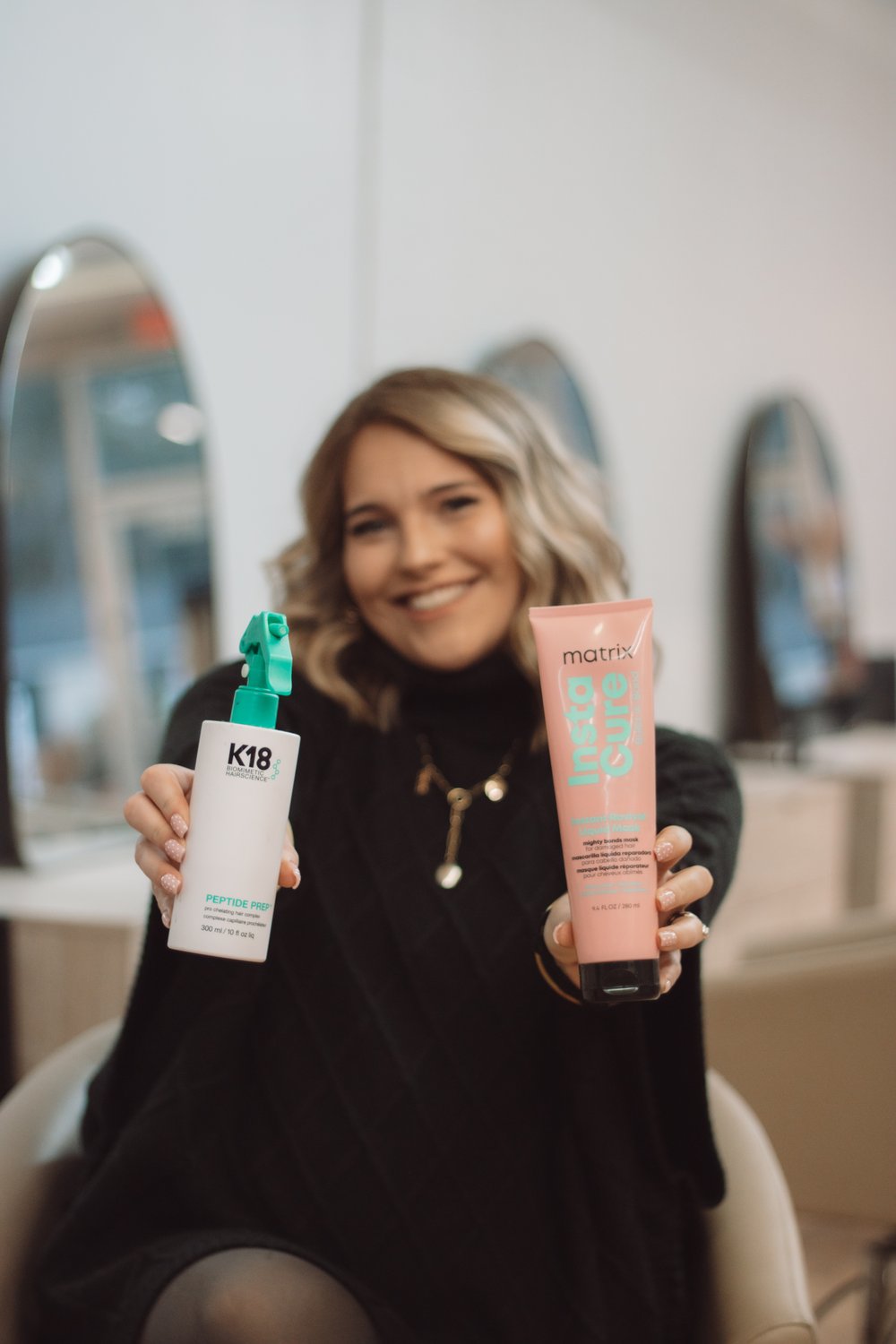 Smiling hairstylist holding up hair care products in her salon