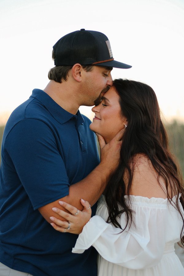 Man kissing his partner on the forehead as she smiles with eyes closed at sunset