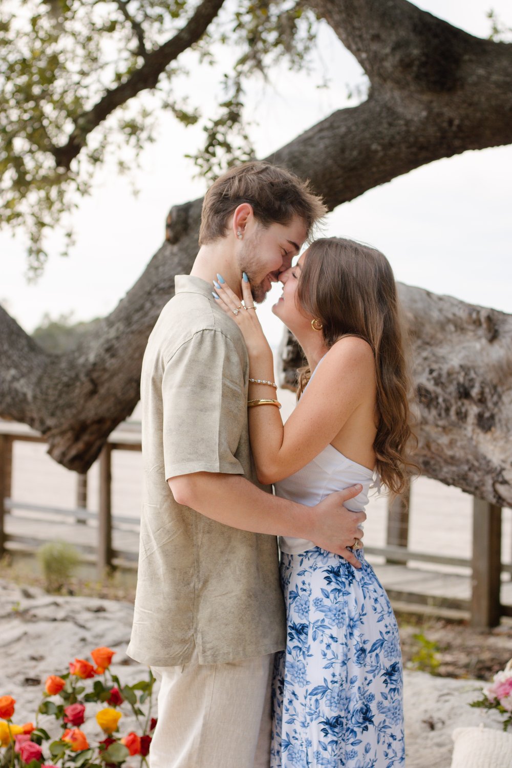 Couple standing nose to nose beneath a sprawling oak tree