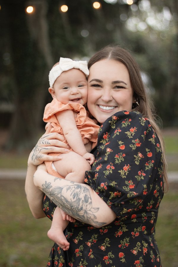 Smiling mother holding her baby cheek to cheek outdoors under string lights