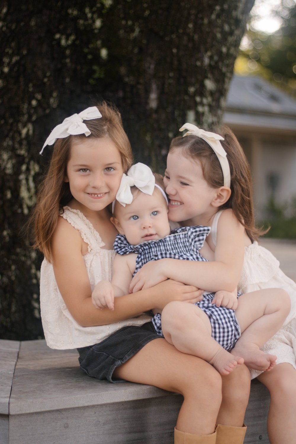 Three young sisters with white bows snuggled together on a bench
