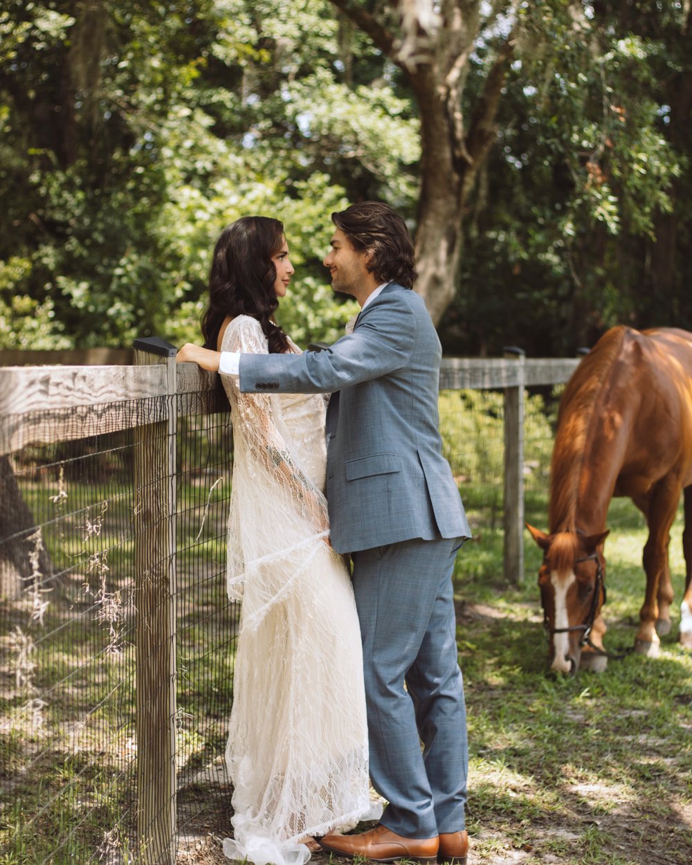Bride and groom leaning on a wooden fence beside a chestnut horse